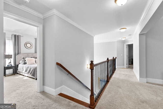 hall with baseboards, ornamental molding, carpet flooring, and an upstairs landing