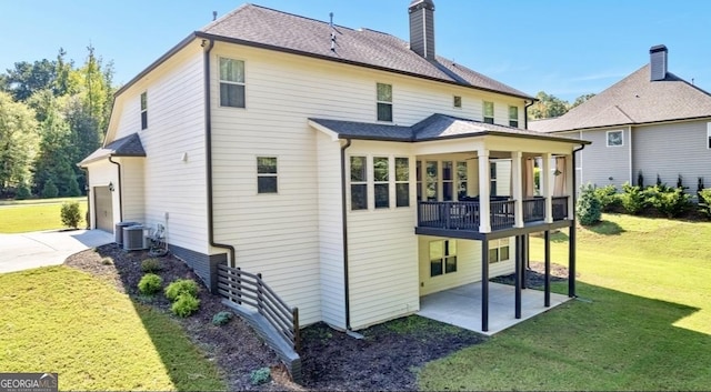 rear view of property with a garage, concrete driveway, a lawn, a chimney, and a patio area