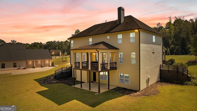 back of house at dusk featuring a patio, a detached garage, fence, a yard, and a chimney