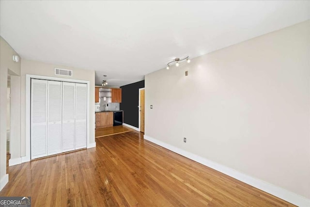 unfurnished living room with baseboards, visible vents, and wood finished floors