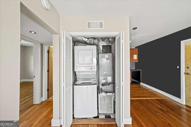 clothes washing area featuring laundry area, baseboards, visible vents, stacked washer and clothes dryer, and wood finished floors