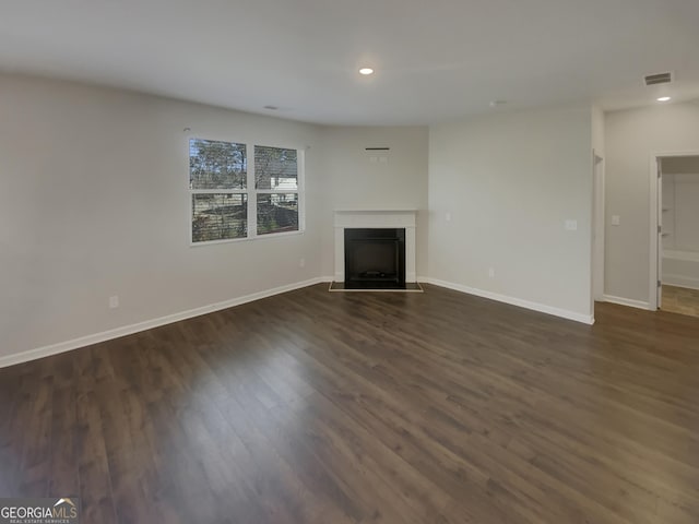 unfurnished living room with baseboards, visible vents, dark wood-type flooring, and a fireplace with flush hearth