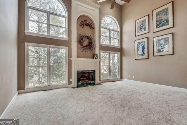 unfurnished living room featuring a fireplace, carpet flooring, a towering ceiling, and baseboards