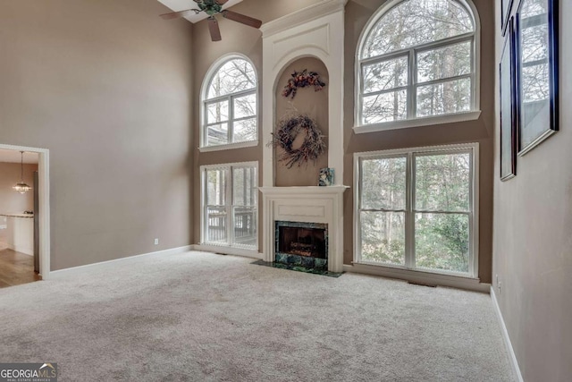 unfurnished living room featuring baseboards, carpet flooring, a towering ceiling, and a high end fireplace