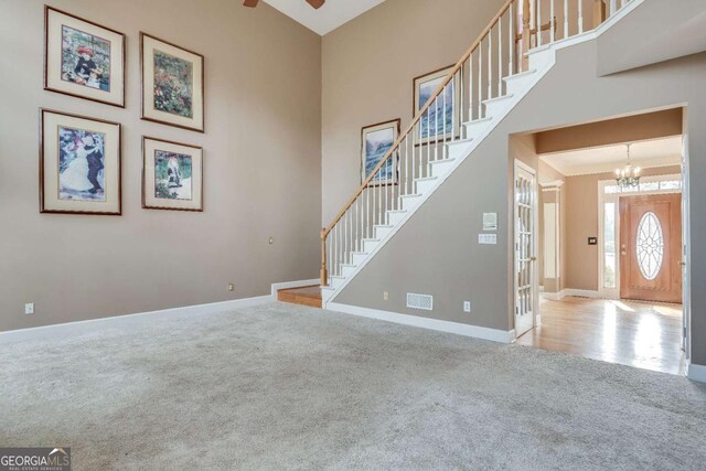 carpeted living room featuring a towering ceiling, stairs, baseboards, and ceiling fan with notable chandelier