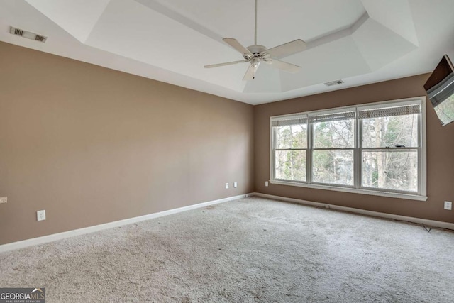 unfurnished room with visible vents, a tray ceiling, baseboards, and carpet flooring