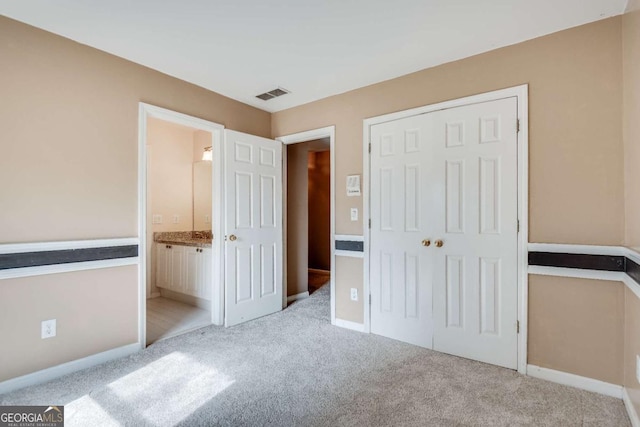 unfurnished bedroom featuring baseboards, visible vents, light colored carpet, ensuite bath, and a closet