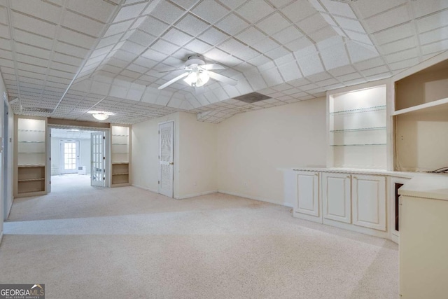 basement featuring built in shelves, baseboards, and light colored carpet