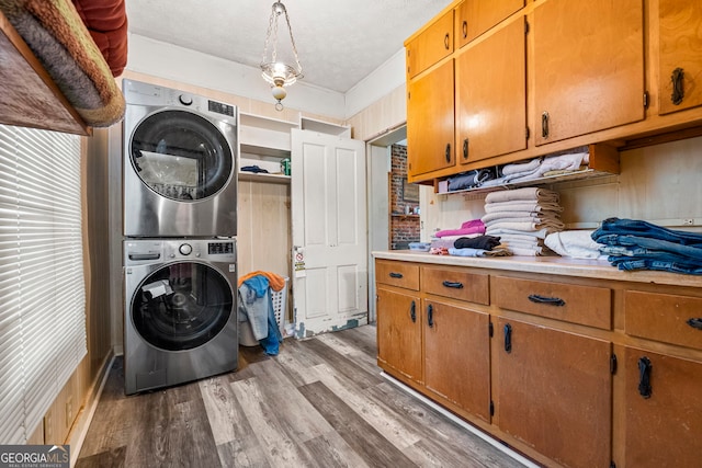 laundry area featuring stacked washer and dryer, cabinet space, light wood-style floors, and a textured ceiling