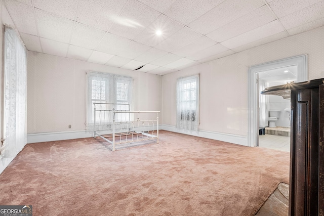 carpeted empty room featuring a drop ceiling and baseboards