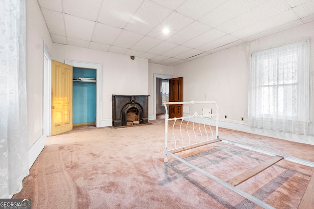 unfurnished living room with baseboards, a drop ceiling, and carpet flooring