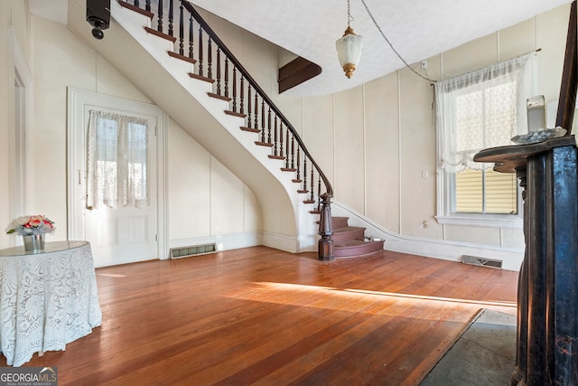 entryway with stairway, visible vents, a decorative wall, and wood finished floors