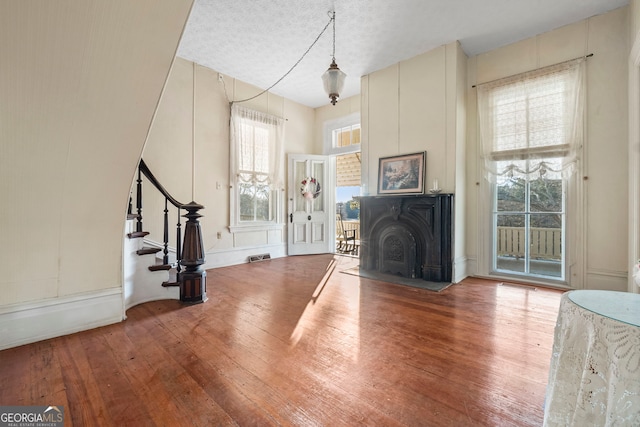 unfurnished living room with wood-type flooring, stairs, visible vents, and a fireplace