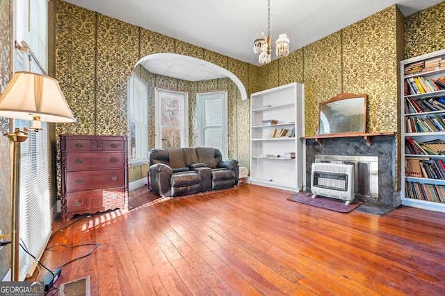 living area with wallpapered walls, visible vents, arched walkways, hardwood / wood-style floors, and heating unit