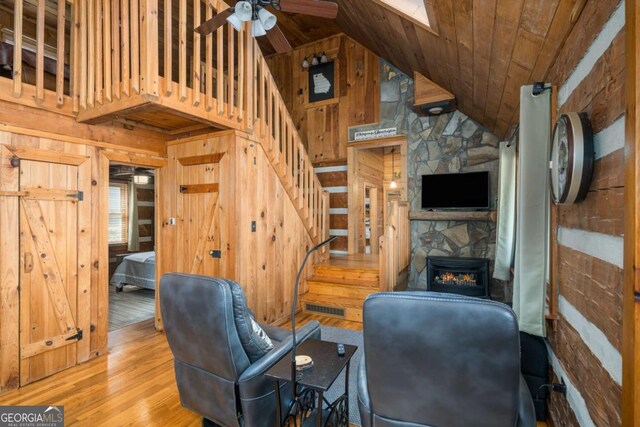 unfurnished living room featuring visible vents, wood finished floors, stairway, wooden walls, and a stone fireplace