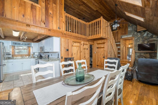 dining space with light wood finished floors, wooden walls, wooden ceiling, and ceiling fan