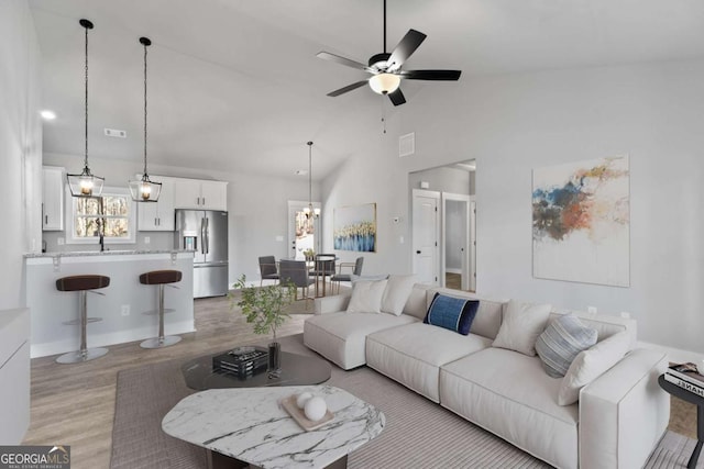 living room with high vaulted ceiling, light wood-type flooring, visible vents, and ceiling fan with notable chandelier