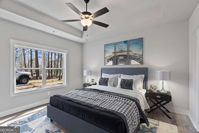 bedroom featuring a raised ceiling, visible vents, a ceiling fan, wood finished floors, and baseboards