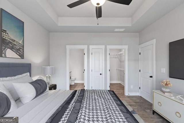 bedroom featuring a walk in closet, a raised ceiling, visible vents, and wood finished floors