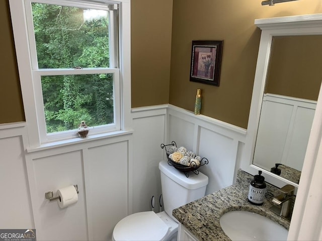 half bathroom with wainscoting, a decorative wall, vanity, and toilet