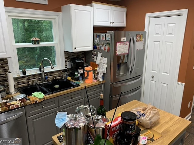 kitchen with decorative backsplash, gray cabinets, stainless steel appliances, white cabinetry, and a sink