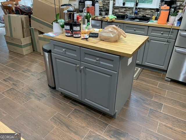 kitchen featuring stone finish floor, gray cabinets, a sink, and wood counters