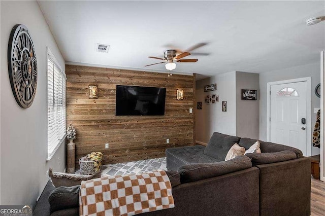 living room with visible vents, a ceiling fan, an accent wall, wood finished floors, and wood walls