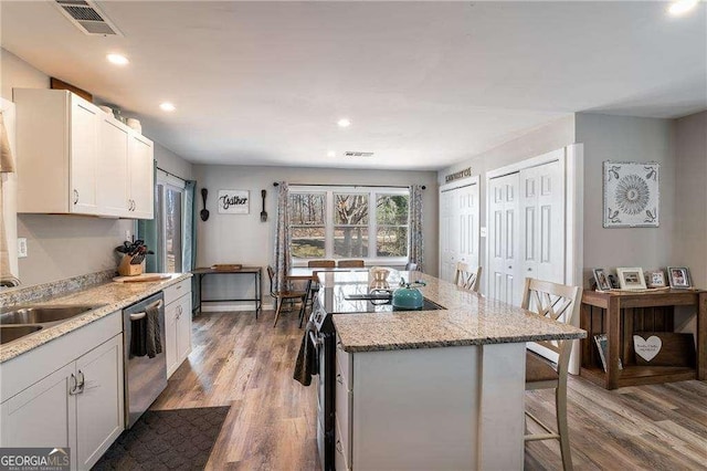 kitchen featuring a sink, visible vents, appliances with stainless steel finishes, a center island, and a kitchen bar