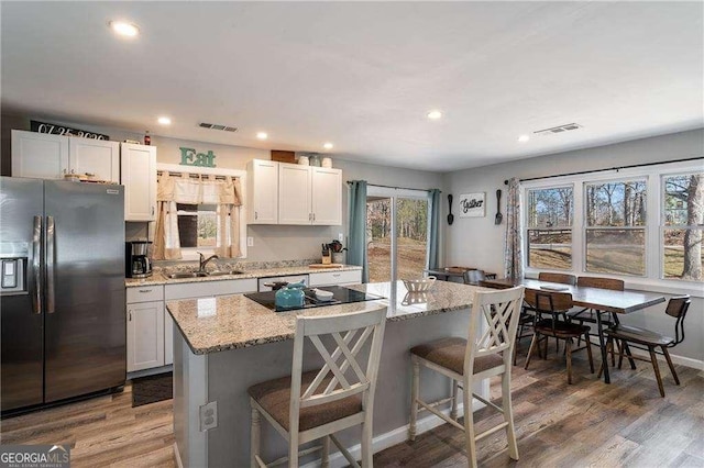 kitchen featuring visible vents, a sink, refrigerator with ice dispenser, and a kitchen bar