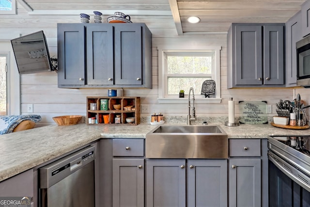 kitchen with light countertops, appliances with stainless steel finishes, a sink, and gray cabinetry