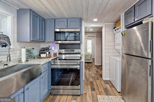 kitchen with stainless steel appliances, stacked washer and dryer, light countertops, dark wood-type flooring, and wood ceiling