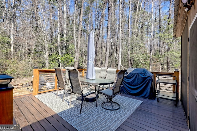 deck featuring a forest view, outdoor dining area, and grilling area