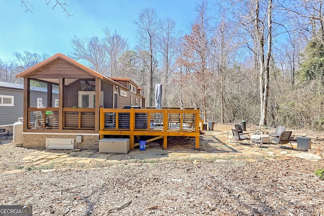 rear view of property featuring a deck, a fire pit, and a sunroom