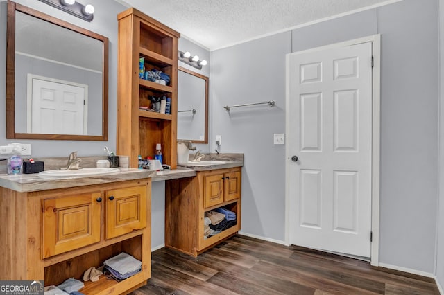 full bath featuring two vanities, a sink, a textured ceiling, and wood finished floors