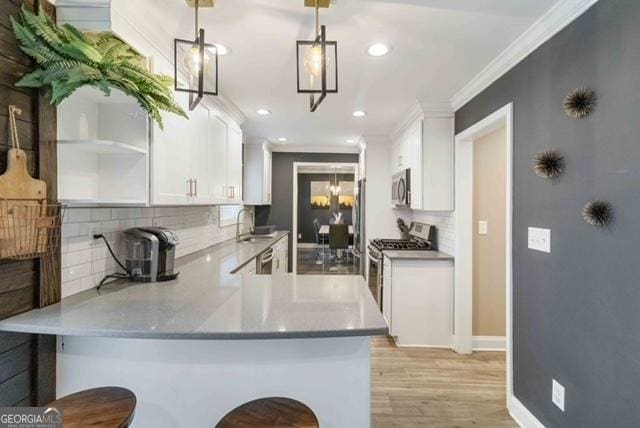 kitchen featuring light wood-style flooring, appliances with stainless steel finishes, a peninsula, crown molding, and white cabinetry