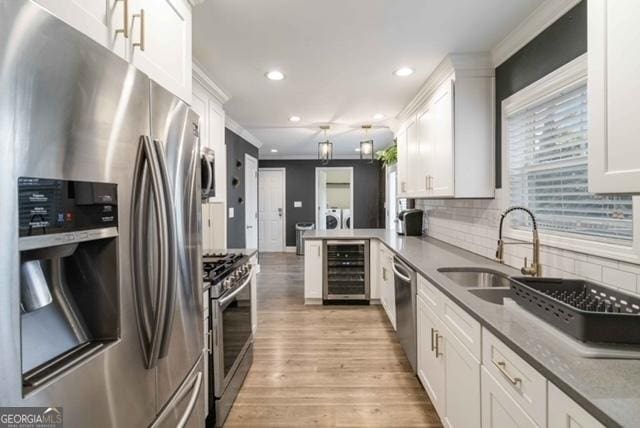 kitchen with beverage cooler, stainless steel appliances, a sink, and white cabinetry