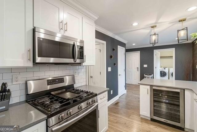 kitchen with beverage cooler, white cabinetry, stainless steel appliances, and washing machine and dryer