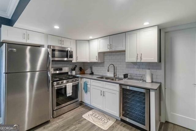 kitchen with wine cooler, a sink, white cabinets, appliances with stainless steel finishes, and light wood-type flooring