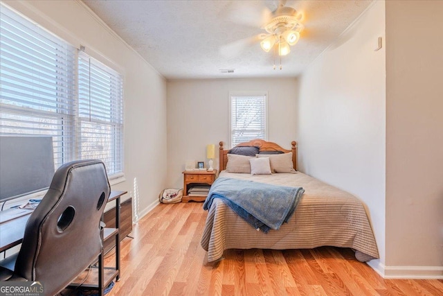 bedroom featuring a textured ceiling, a ceiling fan, baseboards, visible vents, and light wood-style floors