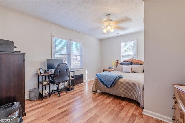 bedroom with a textured ceiling, ceiling fan, baseboards, and light wood-style floors