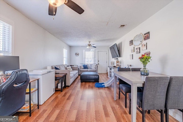 living area featuring light wood finished floors, a ceiling fan, visible vents, and a textured ceiling