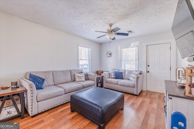 living area featuring light wood-type flooring, a textured ceiling, visible vents, and a ceiling fan