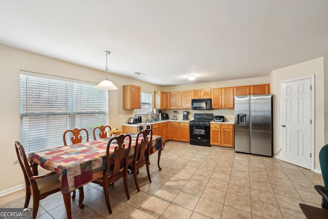 kitchen with light tile patterned floors, decorative light fixtures, a sink, light countertops, and black appliances