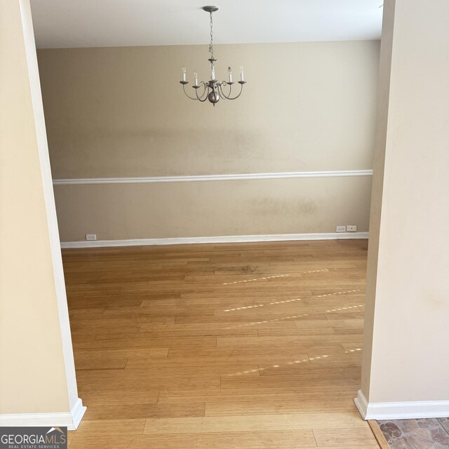 spare room with a chandelier, baseboards, and hardwood / wood-style floors