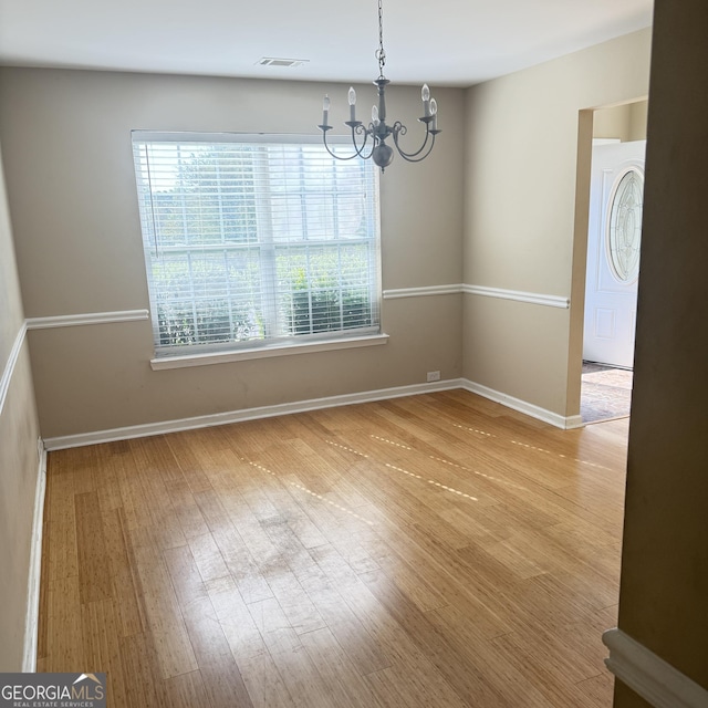 unfurnished dining area with a chandelier, visible vents, baseboards, and wood finished floors