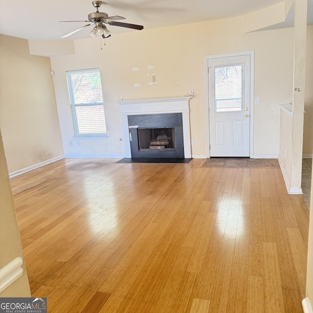 unfurnished living room with baseboards, a fireplace with flush hearth, light wood-type flooring, and a ceiling fan