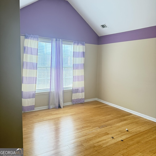 spare room with a wealth of natural light, lofted ceiling, visible vents, and wood finished floors