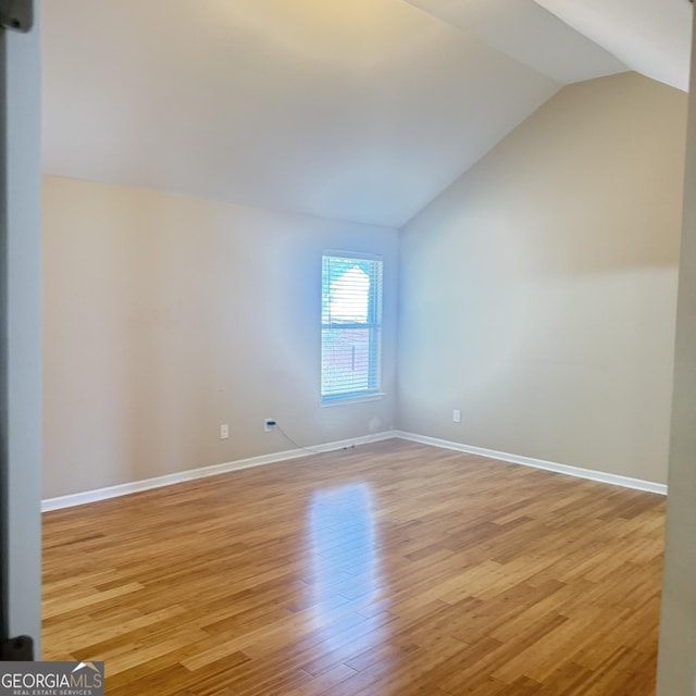 spare room featuring light wood-type flooring, baseboards, and vaulted ceiling