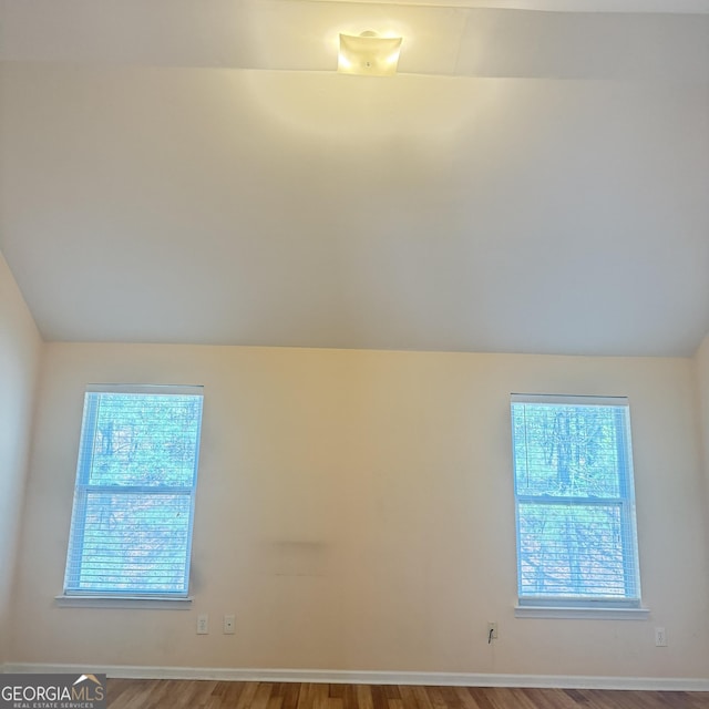 spare room with baseboards, vaulted ceiling, and wood finished floors