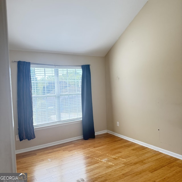 spare room with light wood-style flooring, baseboards, and vaulted ceiling
